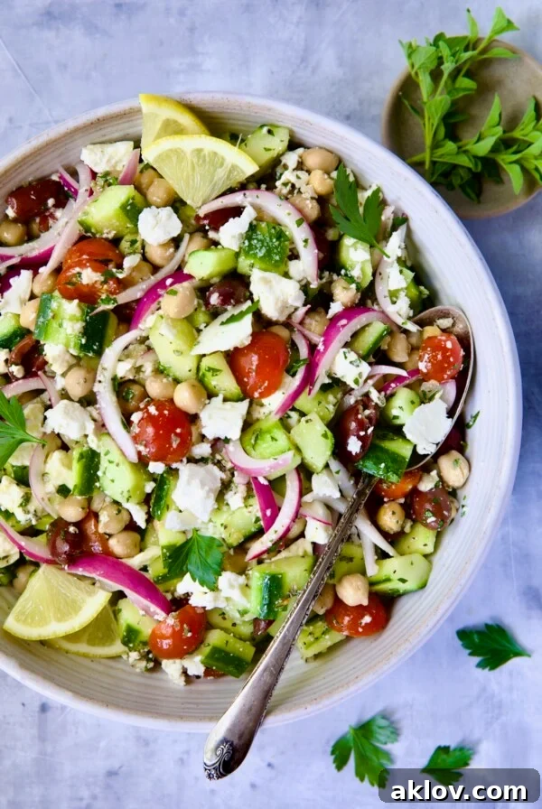 Greek Cucumber Salad in white bowl with serving spoon with oregano and parsley scattered about.