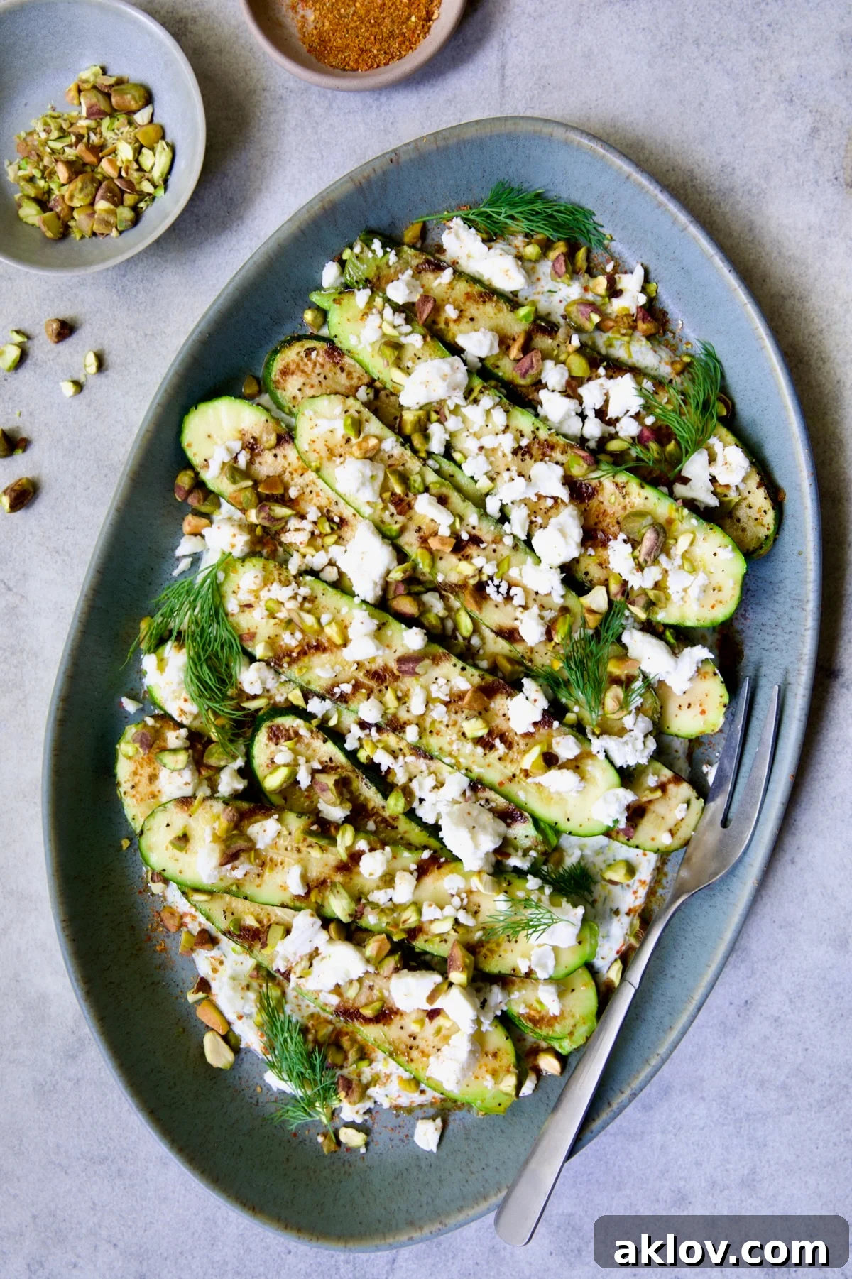 Mediterranean Grilled Zucchini with Dill Yogurt and Feta on blue platter garnished with pistachios and fresh dill sprigs.