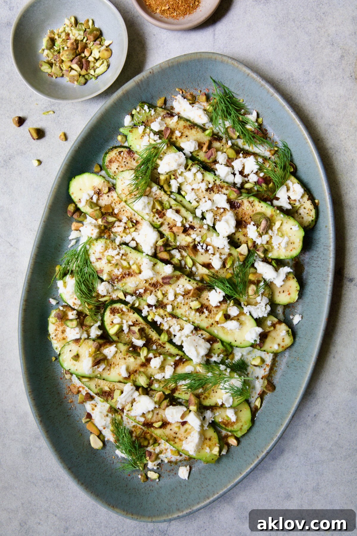 Final presentation of Mediterranean Grilled Zucchini with Dill Yogurt and Feta on a blue platter, beautifully garnished with pistachios and fresh dill sprigs.