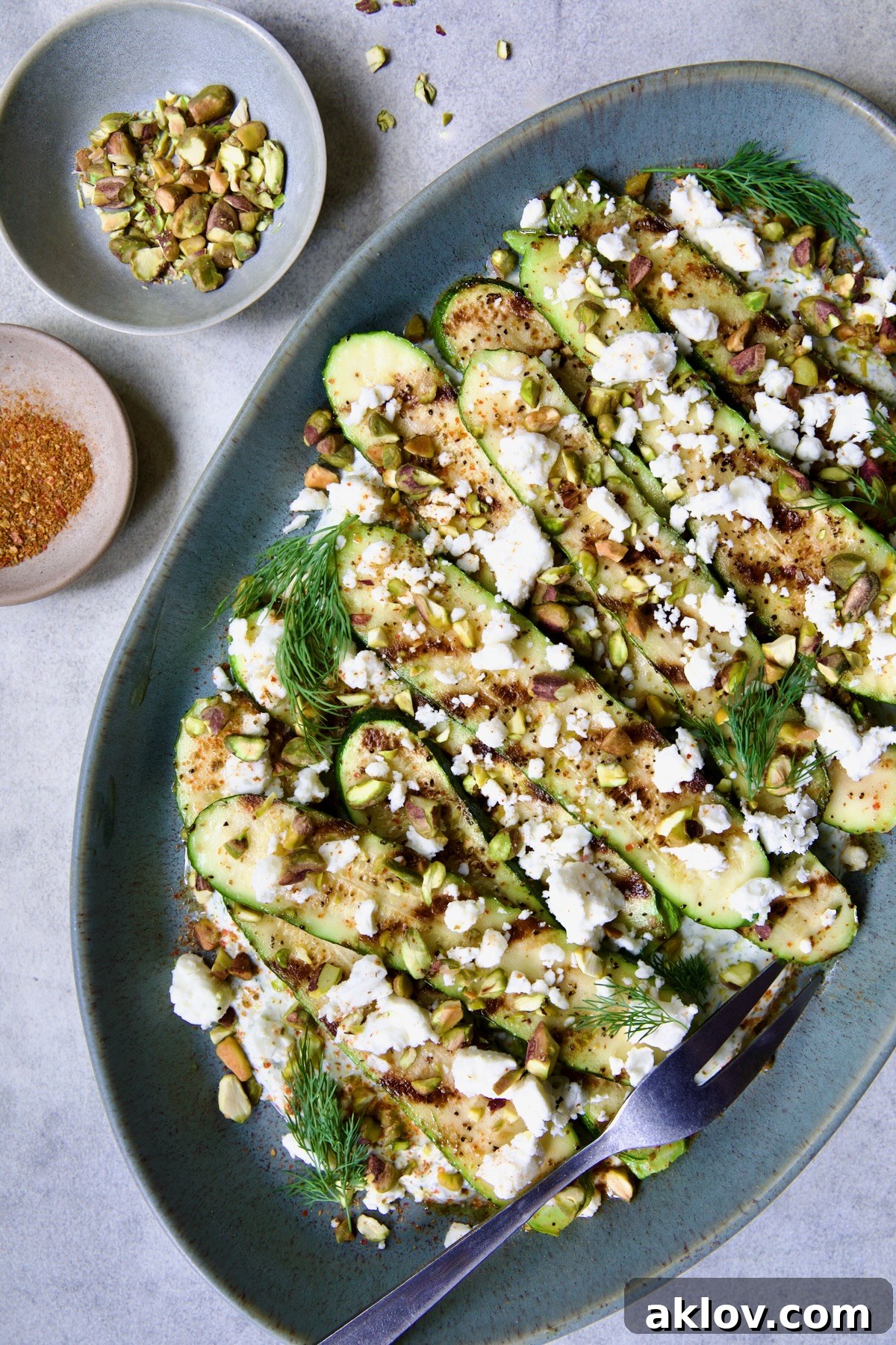 Mediterranean Grilled Zucchini with Dill Yogurt and Feta on blue platter garnished with pistachios and fresh dill sprigs.