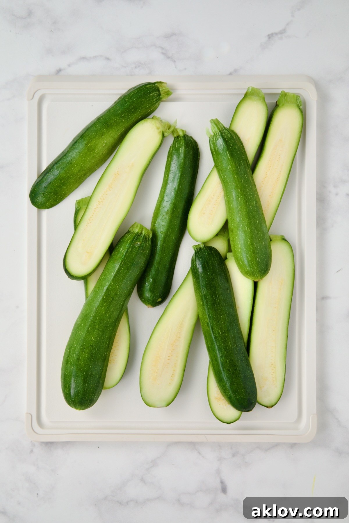 Fresh zucchini sliced into uniform planks on a white cutting board, prepared for grilling.