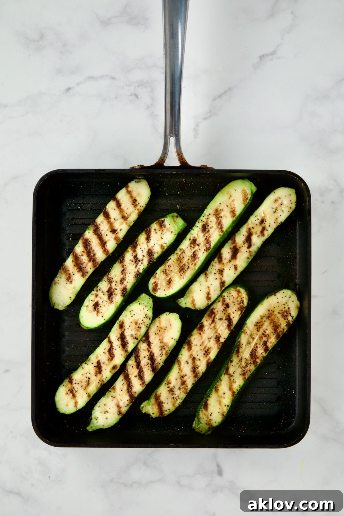 Eight perfectly grilled zucchini slices arranged on a square grill pan, showing appealing char marks.