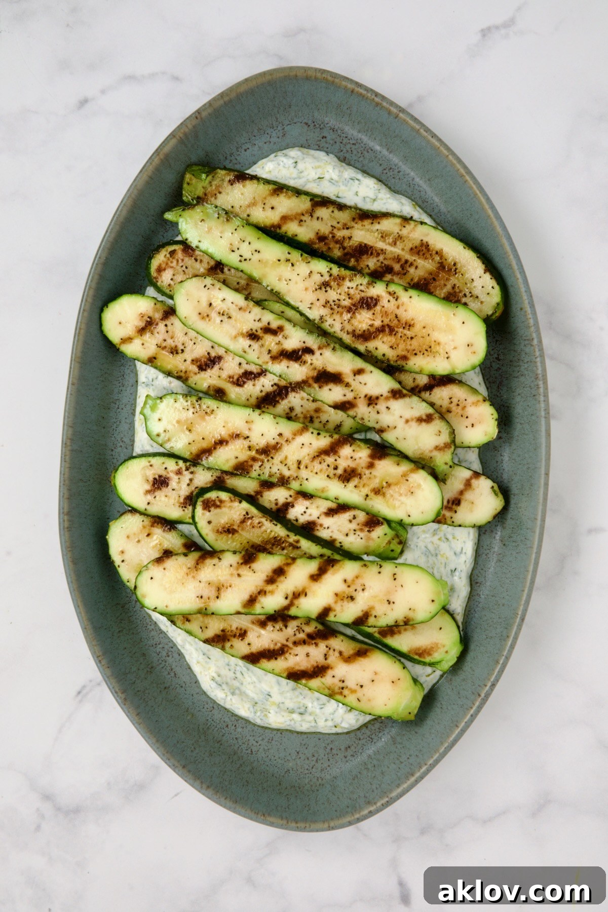 Grilled zucchini slices placed over dill yogurt on blue platter.