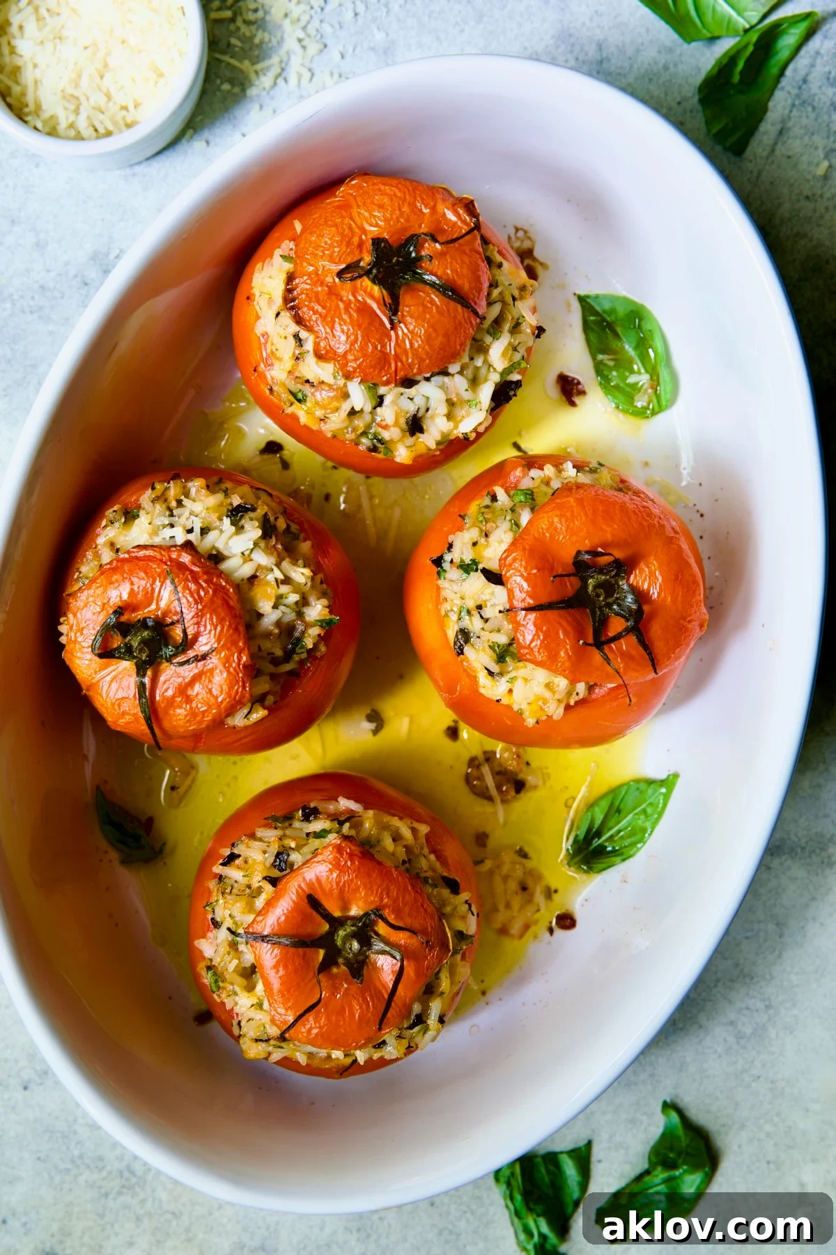 Four Cheesy Rice Stuffed Tomatoes in white oval baking dish, garnished with fresh basil.