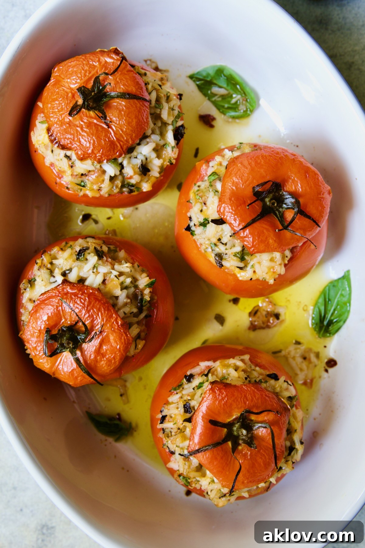 Four Cheesy Rice Stuffed Tomatoes in white oval baking dish with fresh basil leaves for garnish.