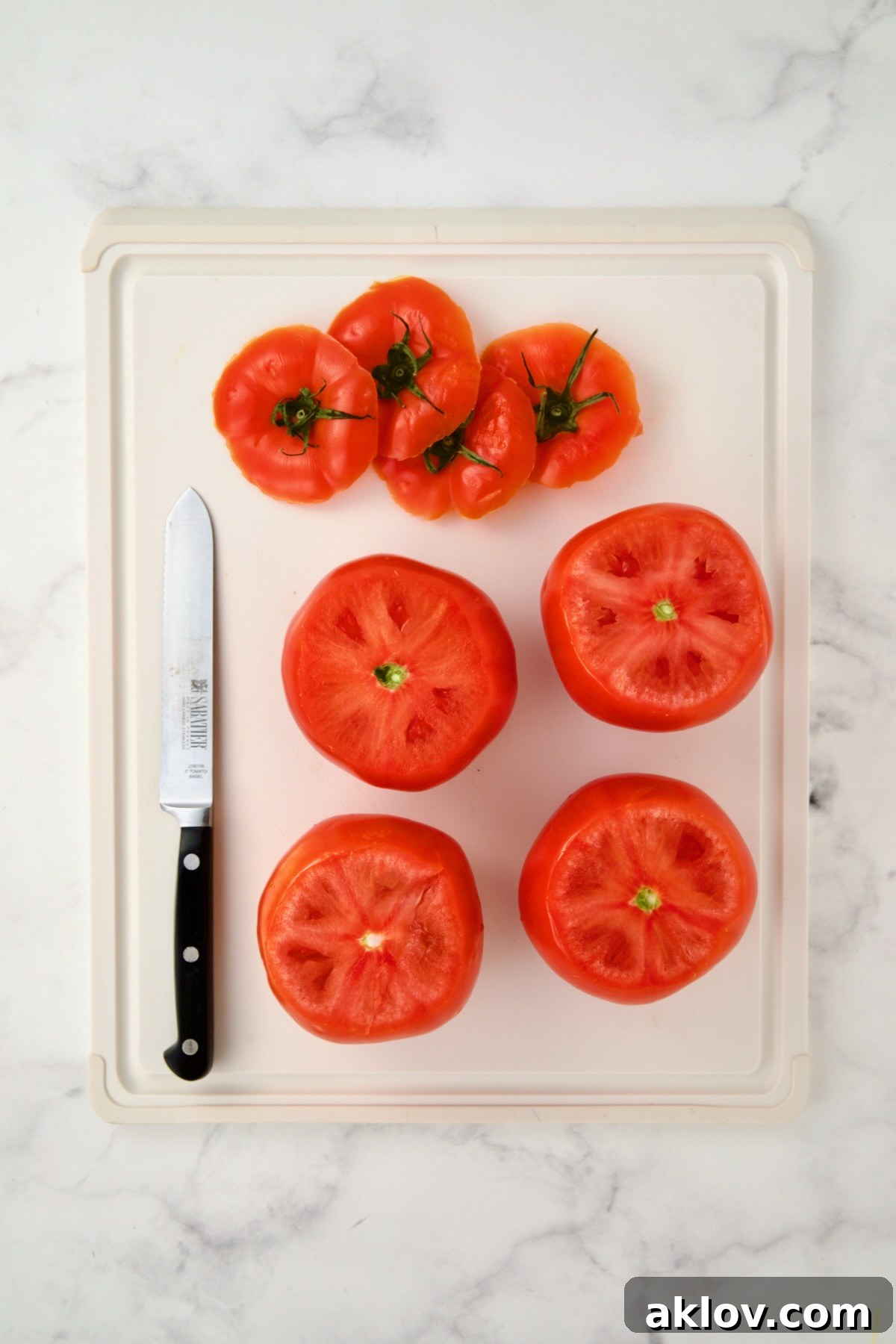 Four round tomatoes with the tops sliced off, neatly arranged on a white plastic cutting board.