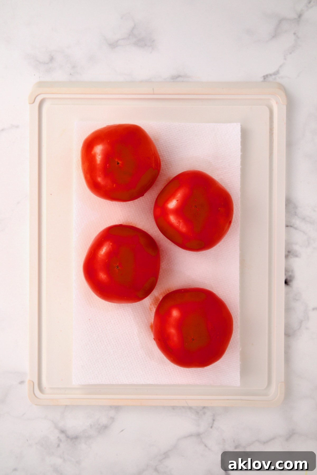 Four round tomatoes inverted onto paper towels on a white plastic cutting board, draining excess liquid.