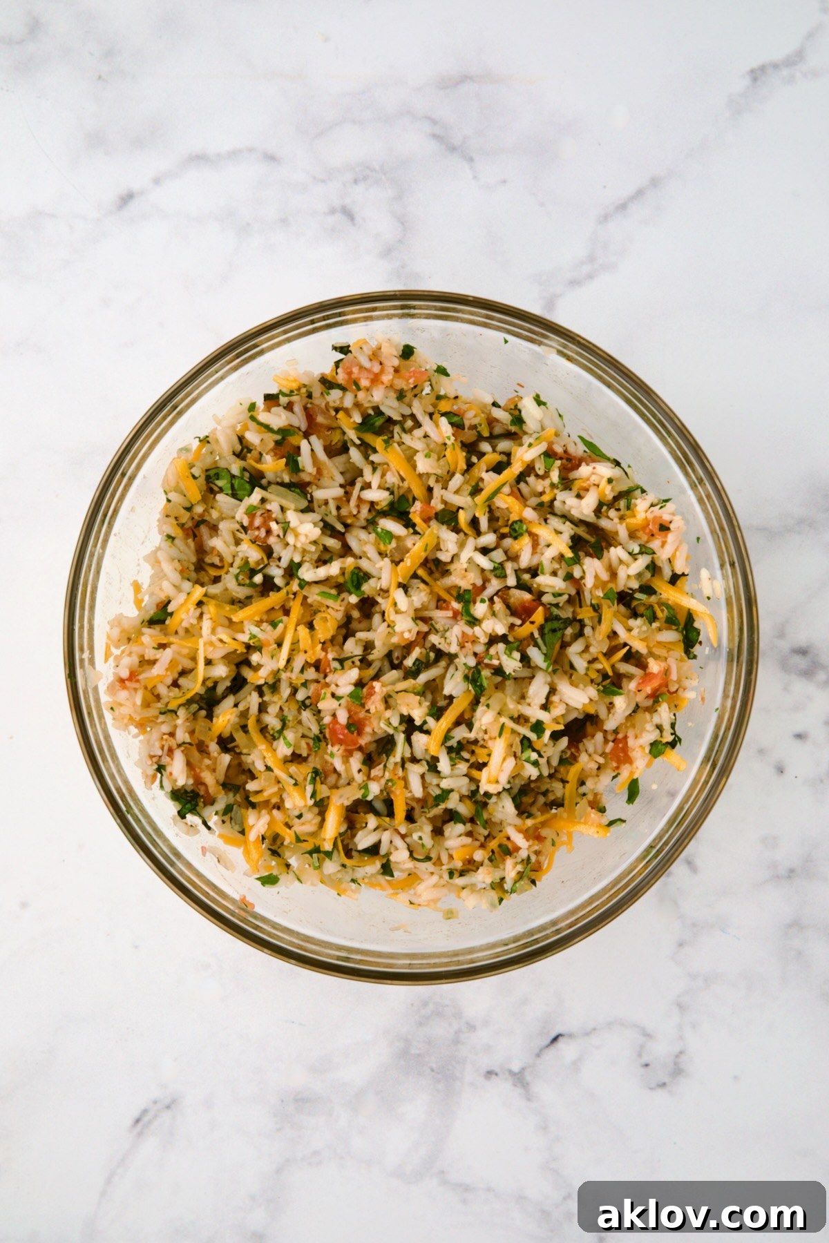 Filling for Cheesy Rice Stuffed Tomatoes in a glass bowl after being mixed together, showing vibrant herbs and cheese.
