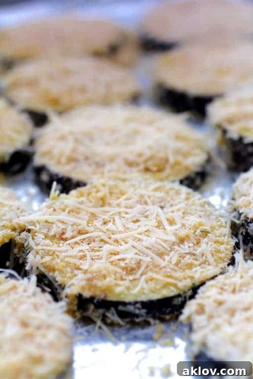 Photo of eggplant slices perfectly coated with breading and Parmesan cheese, arranged neatly on a baking sheet, ready for baking.