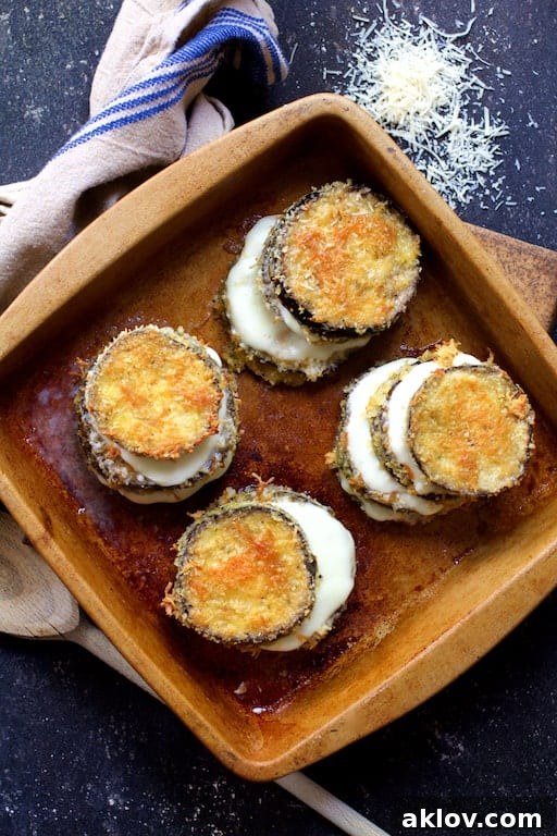 Top-down photo of three eggplant stacks adorned with perfectly melted cheese between the layers, nestled in a clay baking dish.