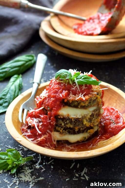 Photo of Eggplant Parmesan Stacks artfully arranged in a wooden bowl, generously topped with savory tomato sauce and garnished with fresh basil.