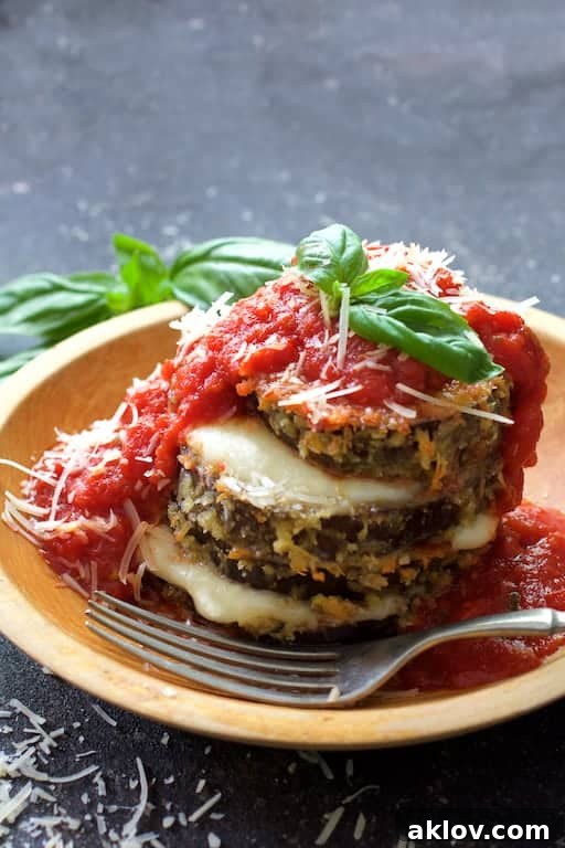 Close-up photo of a single Eggplant Parmesan Stack in a wooden bowl, beautifully garnished with fresh basil, with a fork poised to take the first bite.