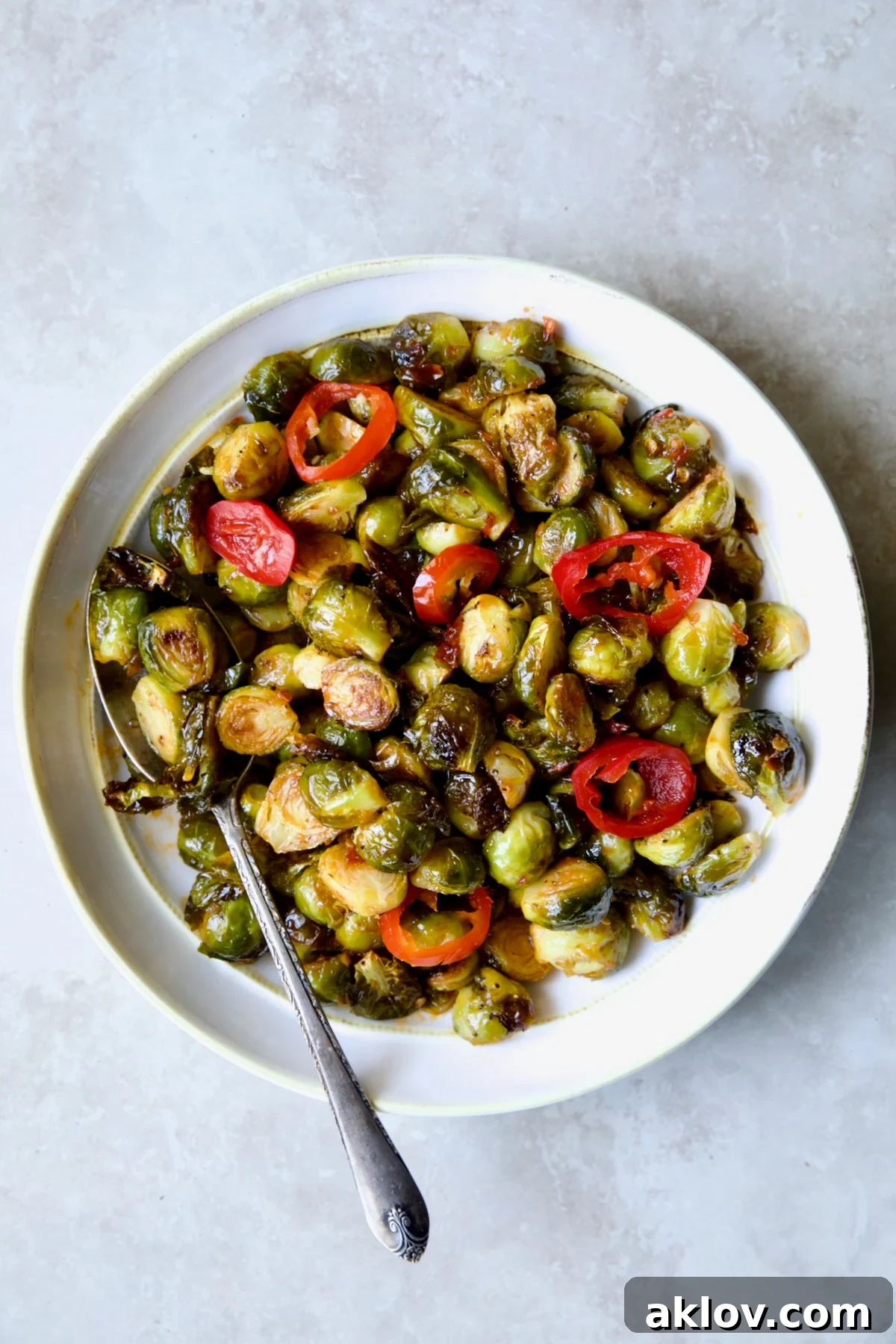 Hot Honey Brussels Sprouts in white serving bowl with serving spoon. Crispy, golden-brown Brussels sprouts glistening with hot honey.