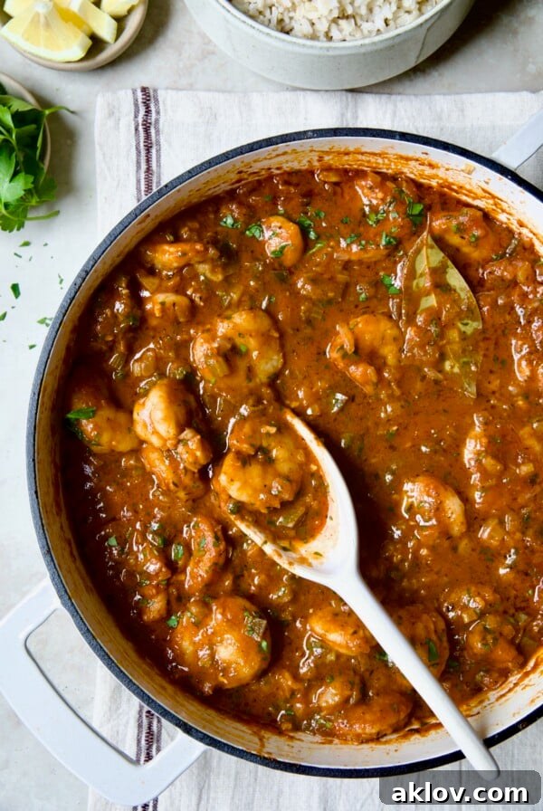 Finished Best Shrimp Creole in a white enamel cast iron skillet with a serving spoon, vibrant and ready to be enjoyed.