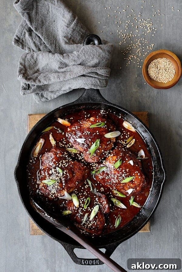 Korean Braised Chicken Thighs in a cast iron skillet, garnished with fresh scallions and sesame seeds.