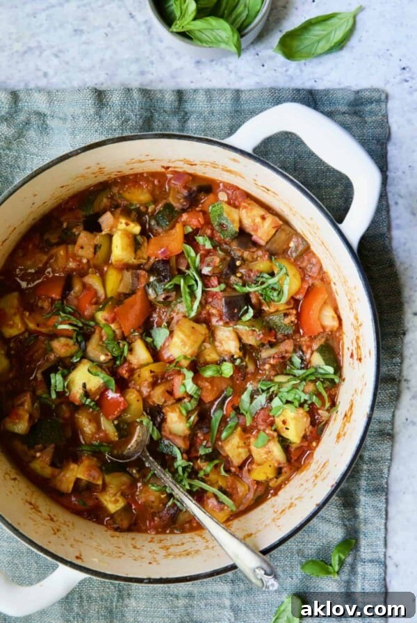 Classic French Ratatouille in a white Dutch oven, garnished with fresh basil leaves, ready to serve.