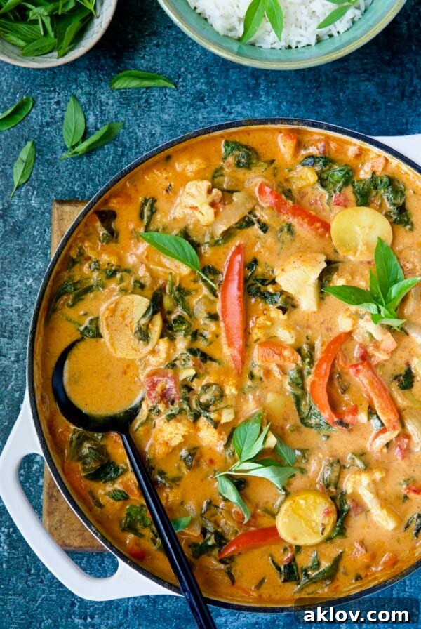 Vegan Thai Red Curry in a white enamel cast iron skillet with a black serving spoon, brimming with colorful vegetables.