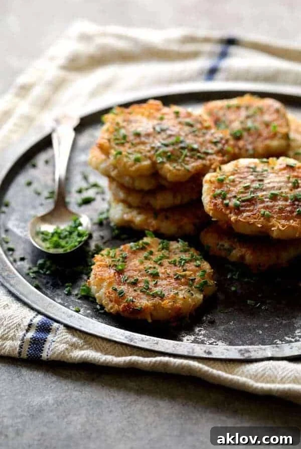 Parmesan Crusted Smashed Turnips, stacked on a metal tray and garnished with fresh chives, ready to serve.