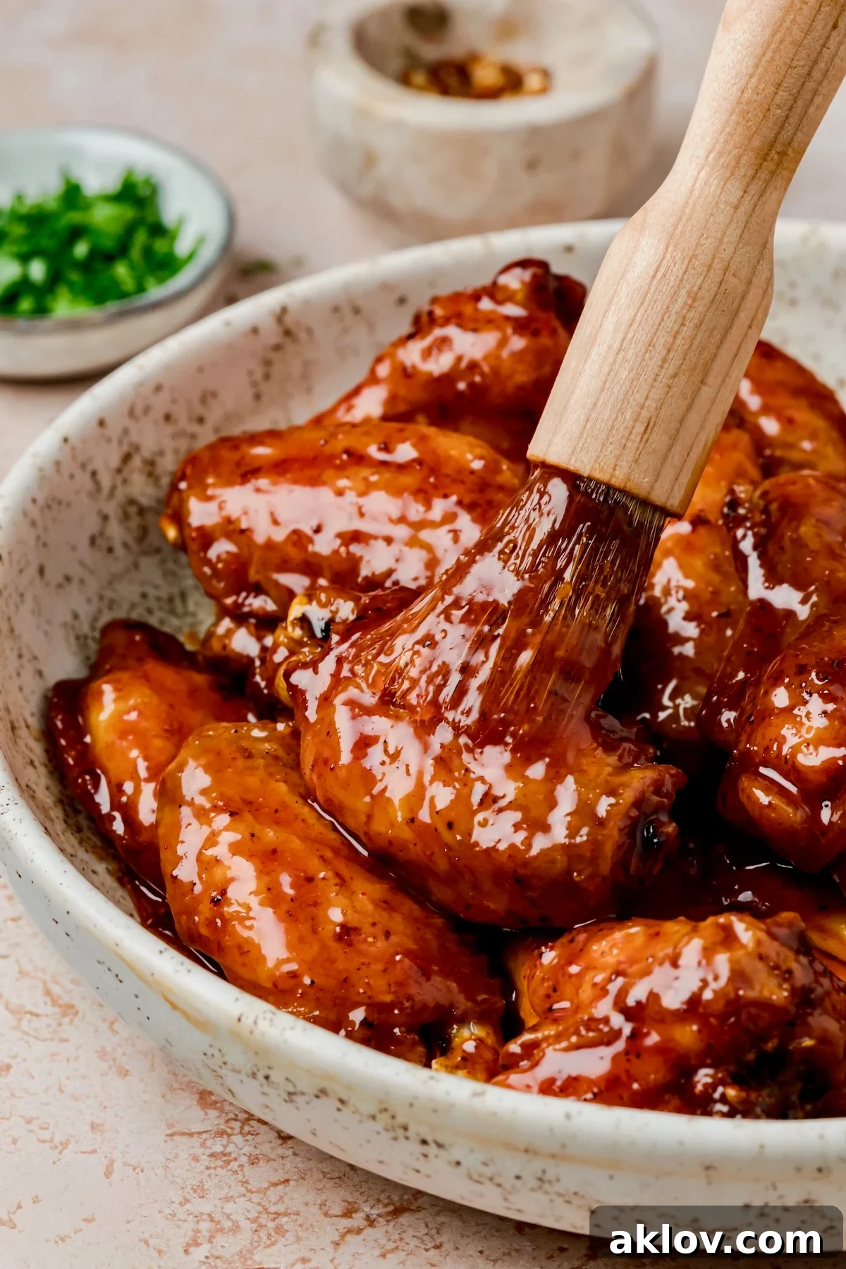 Hot Honey Chicken Wings in speckled bowl being brushed with glass with basting brush.