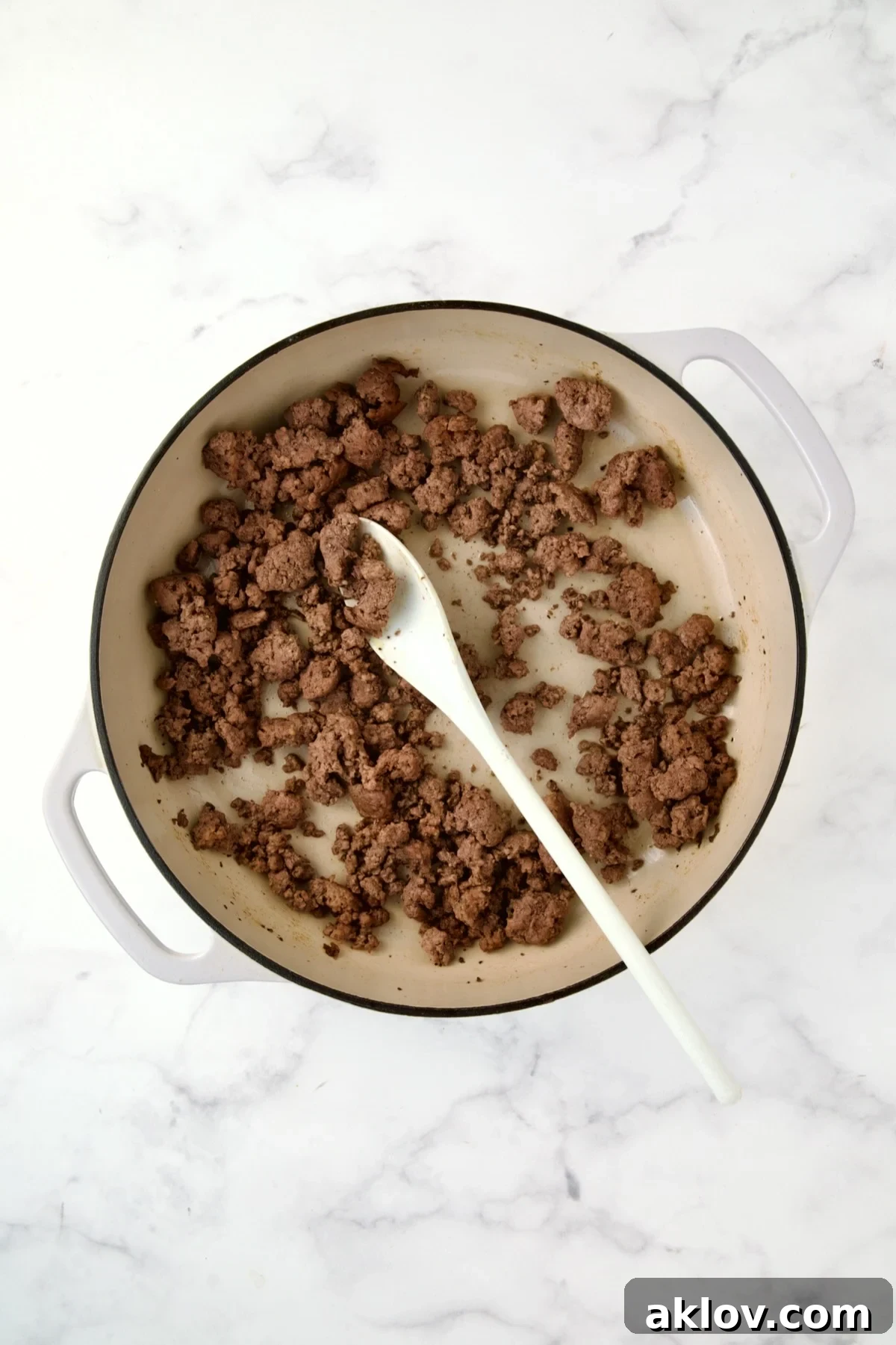 Perfectly browned ground beef resting in a white enamel cast iron skillet.