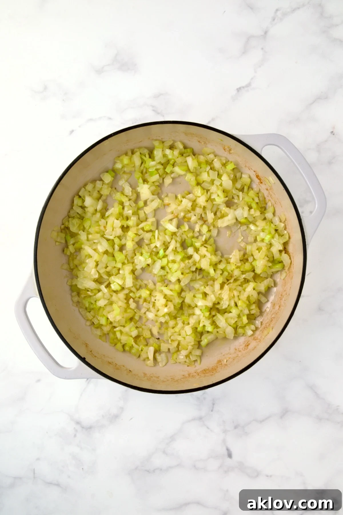 Sautéed onions and celery glistening in a white enamel cast iron skillet.
