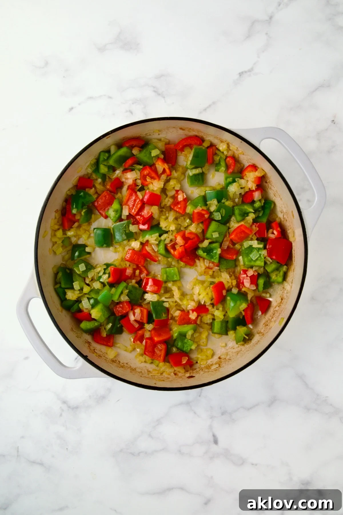 Colorful blend of cooked onions, celery, and bell peppers in a white enamel cast iron skillet.