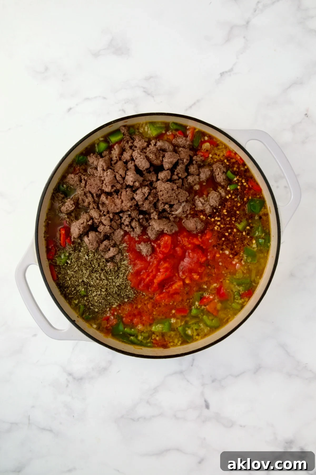 All the simmering ingredients for Unstuffed Peppers Skillet, including broth, tomatoes, and spices, added to cooked vegetables in a white enamel cast iron skillet.