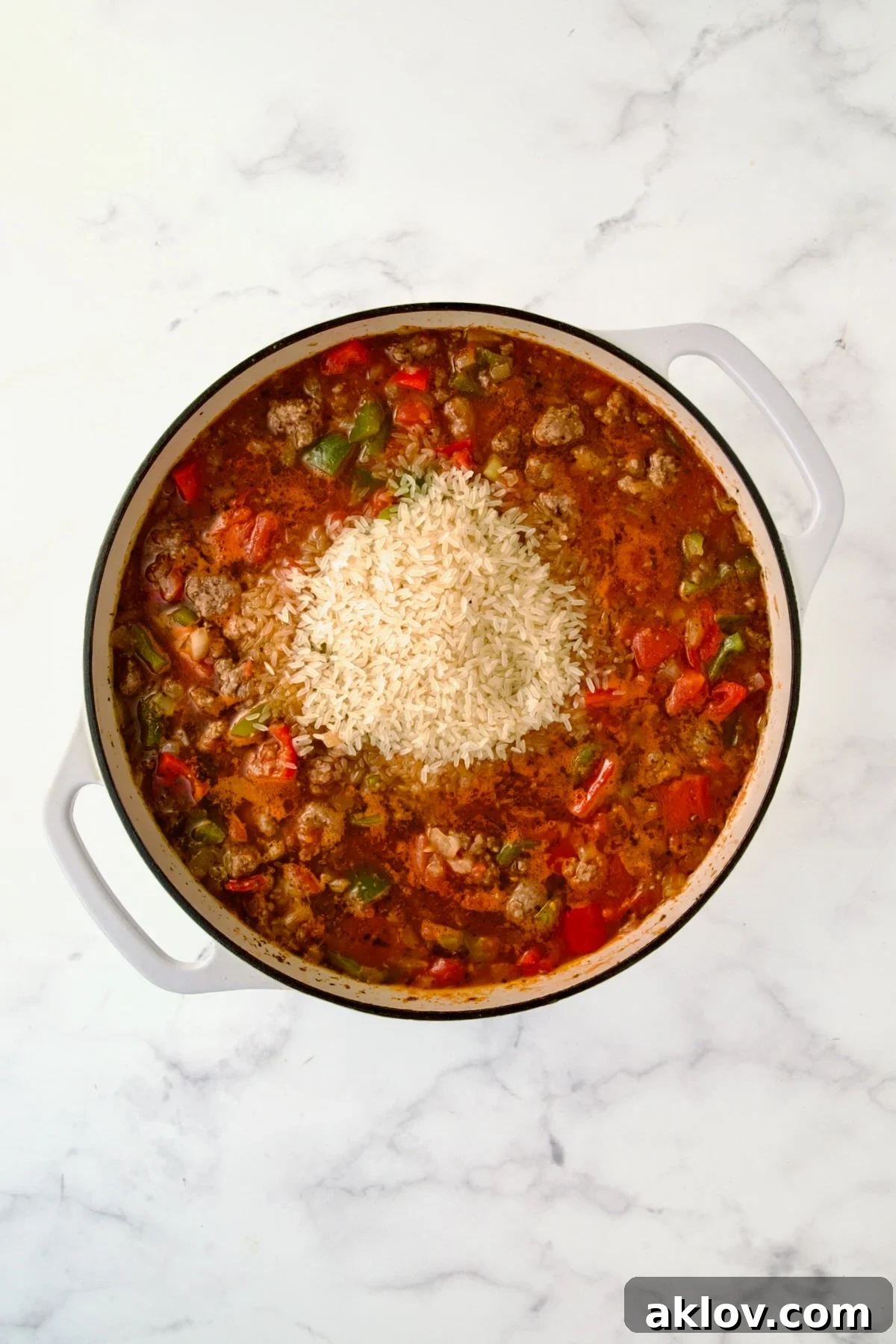 Converted rice incorporated into the simmering ingredients in a white enamel cast iron skillet.