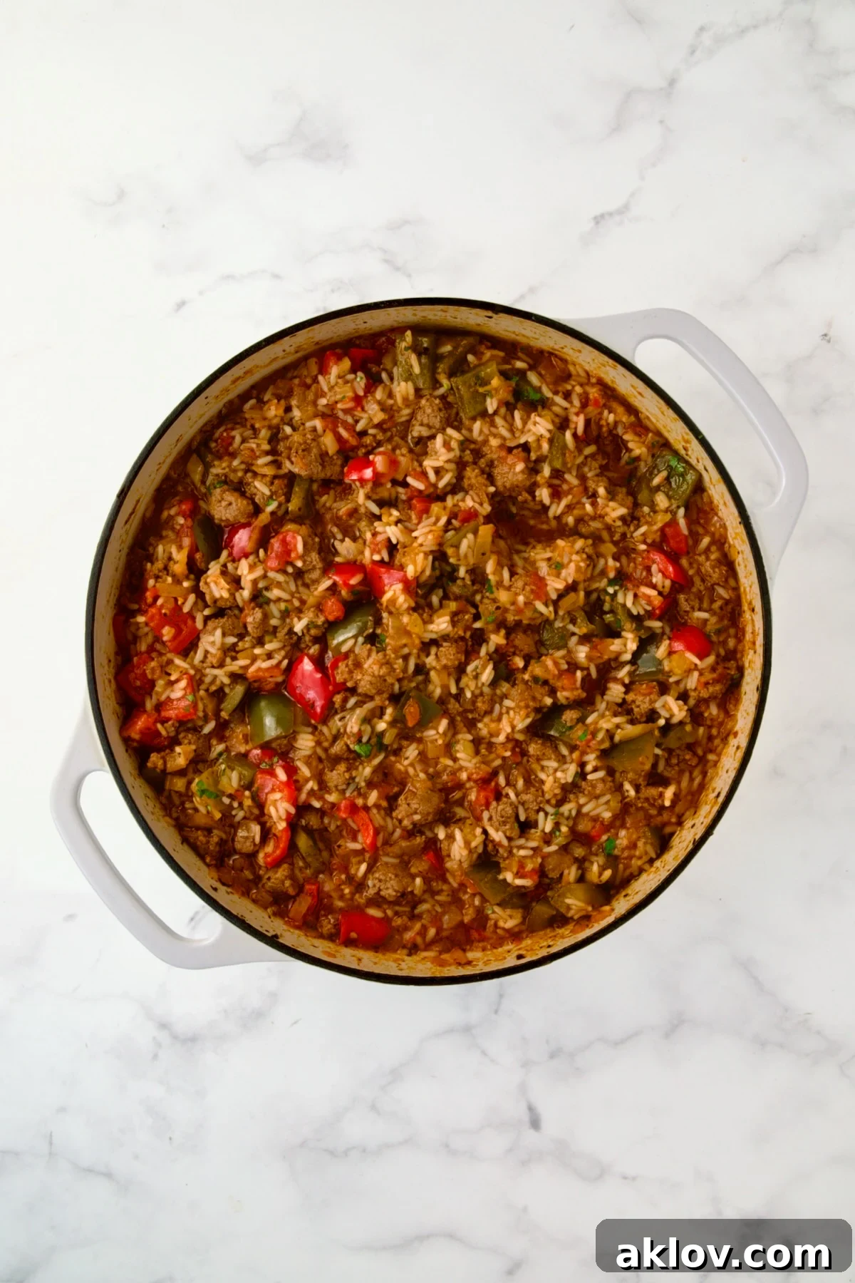 Fully cooked rice, browned beef, and tender vegetables blended in a rich sauce in a white enamel cast iron skillet, ready for cheese.