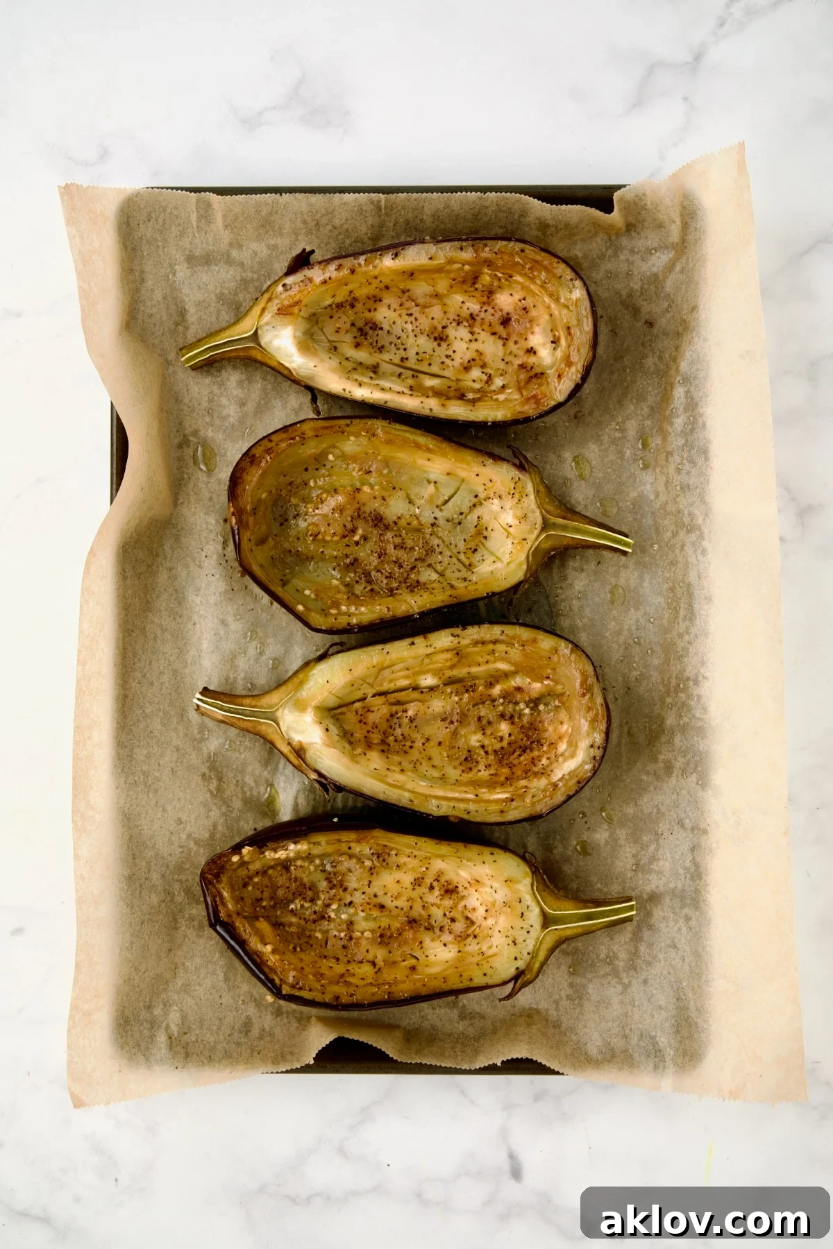 Four baked eggplant halves with pulp side up after being baked on parchment paper lined baking sheet.