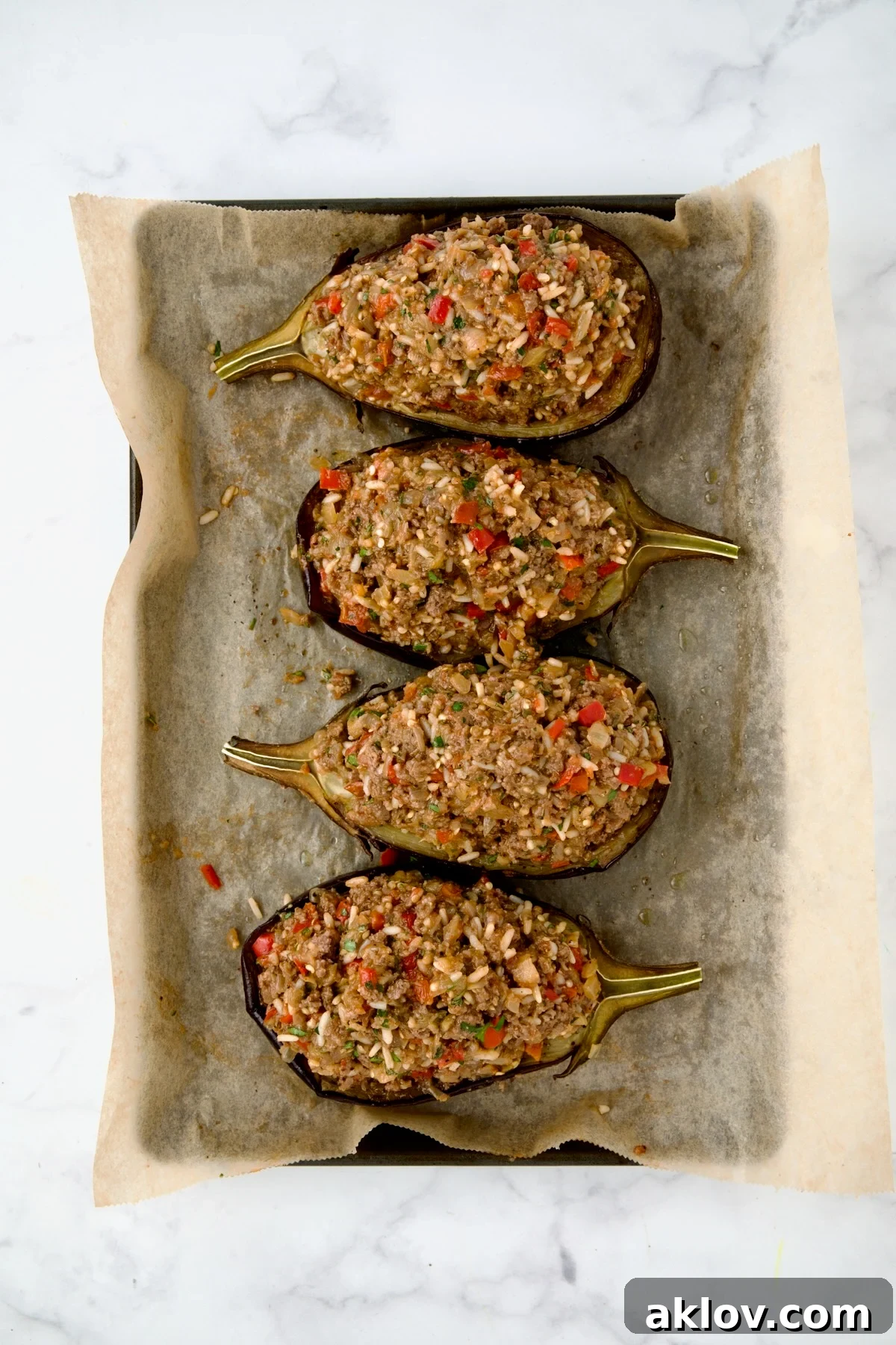 Four stuffed eggplant halves on parchment paper lined baking sheet ready to go into baking pan.