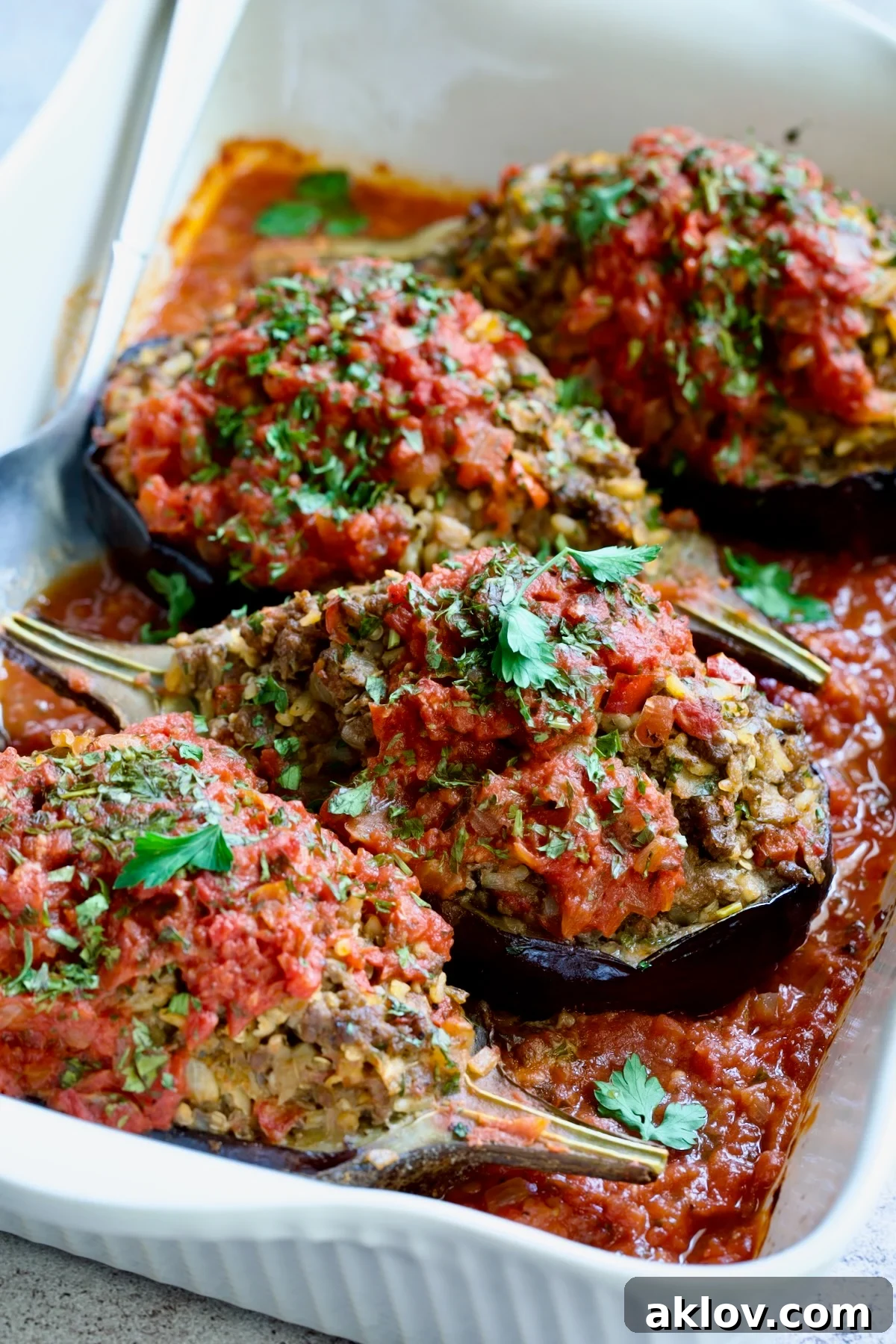 Four baked Stuffed Eggplant halves in white rectangular baking dish with serving spoon.