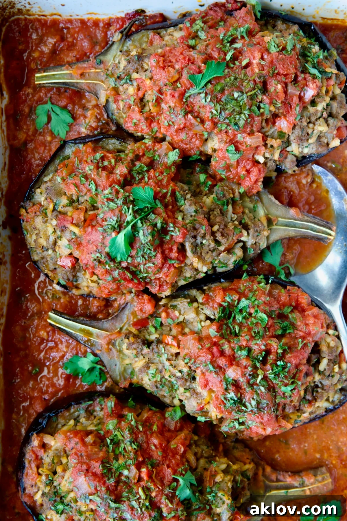 Four baked Stuffed Eggplant halves in white rectangular baking dish with serving spoon.