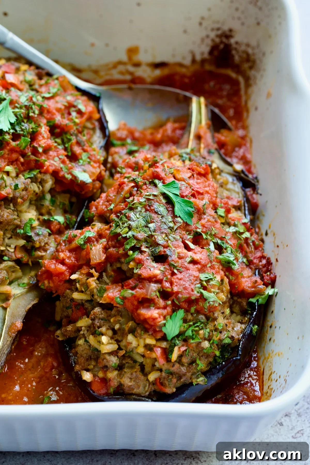 Close-up of one Stuffed Eggplant in white rectangular baking dish with serving spoon.