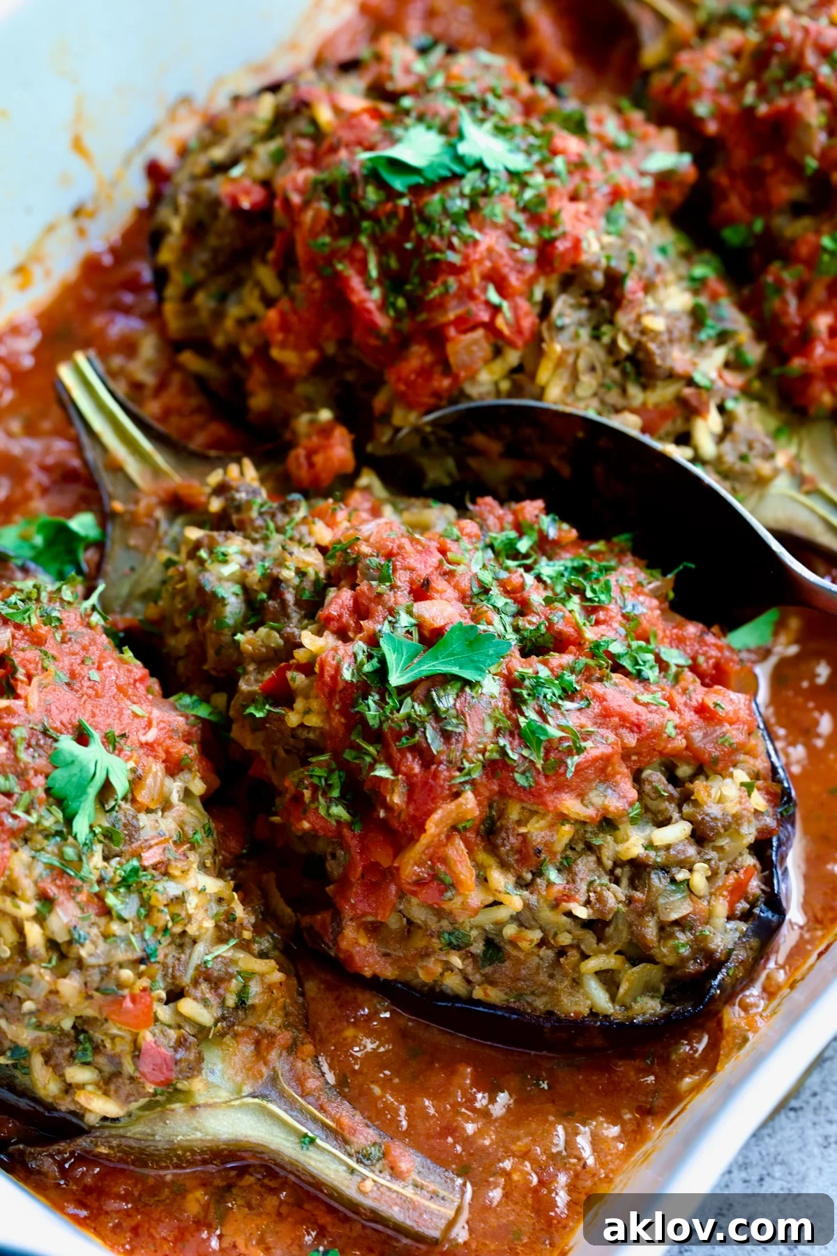 Three baked Stuffed Eggplant halves in white rectangular baking dish with serving spoon.