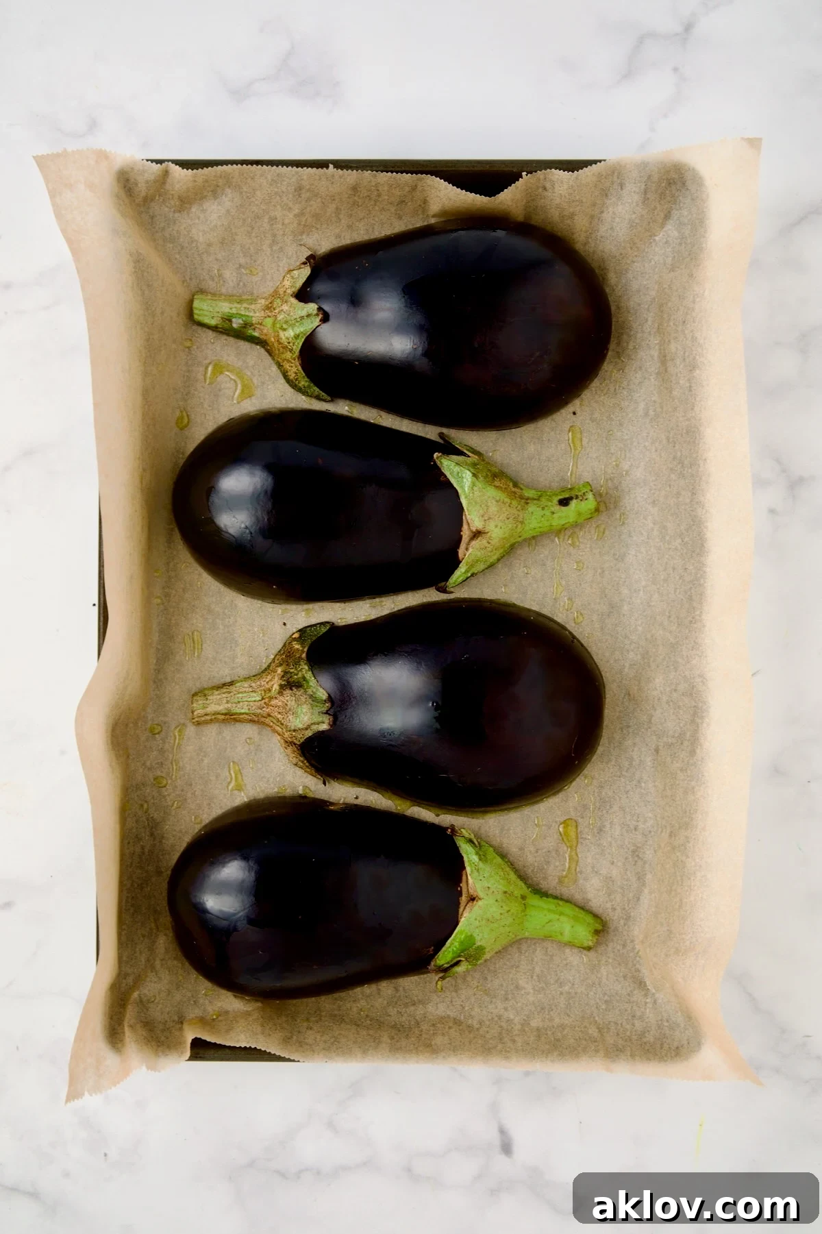 Four eggplant halves with skin side up on parchment paper lined rimmed baking sheet.