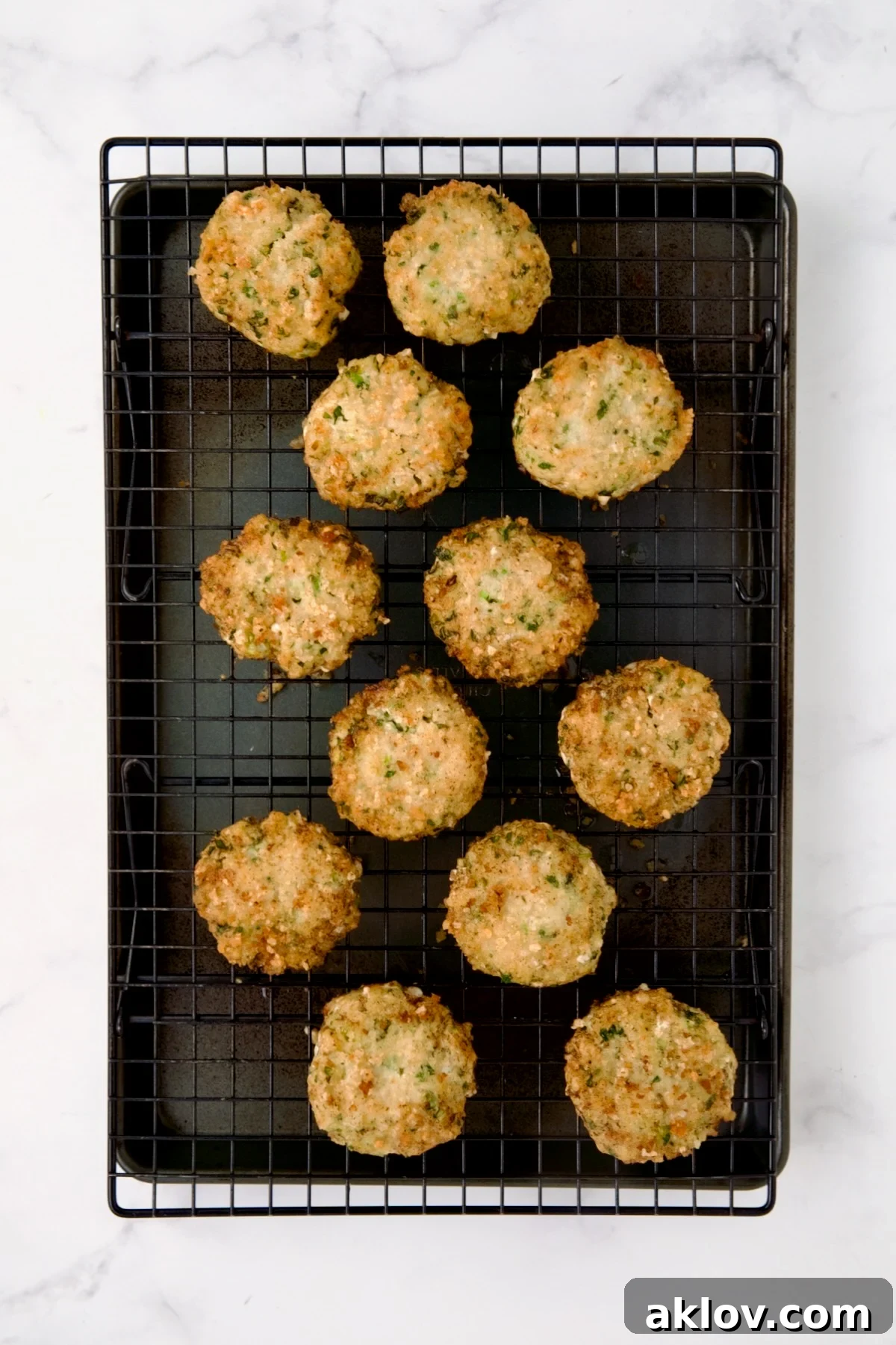 12 cooked shrimp cakes on cooling rack set over a rimmed sheet pan.