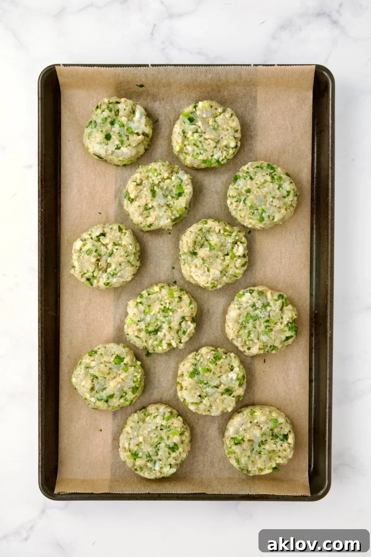 12 uncooked shrimp cakes on parchment paper lined rimmed baking sheet.
