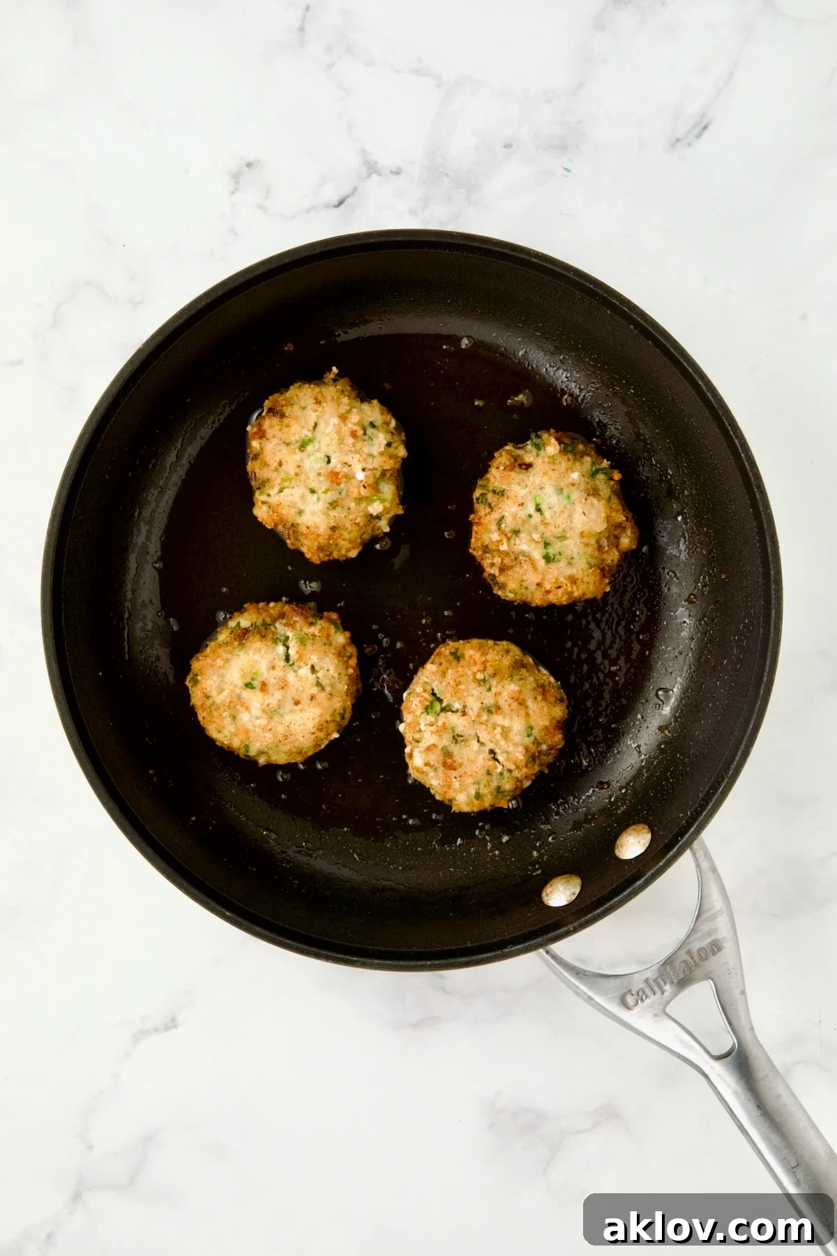 Four cooked shrimp cakes in nonstick skillet.