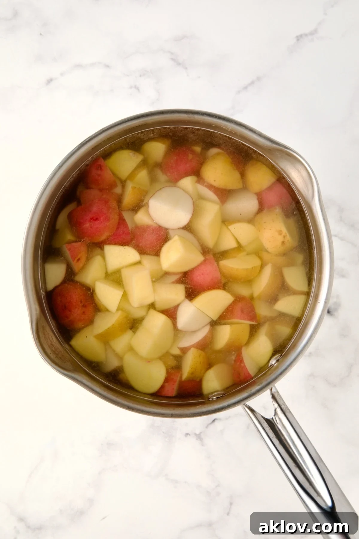 Cubed red and yellow potatoes in water in saucepan.