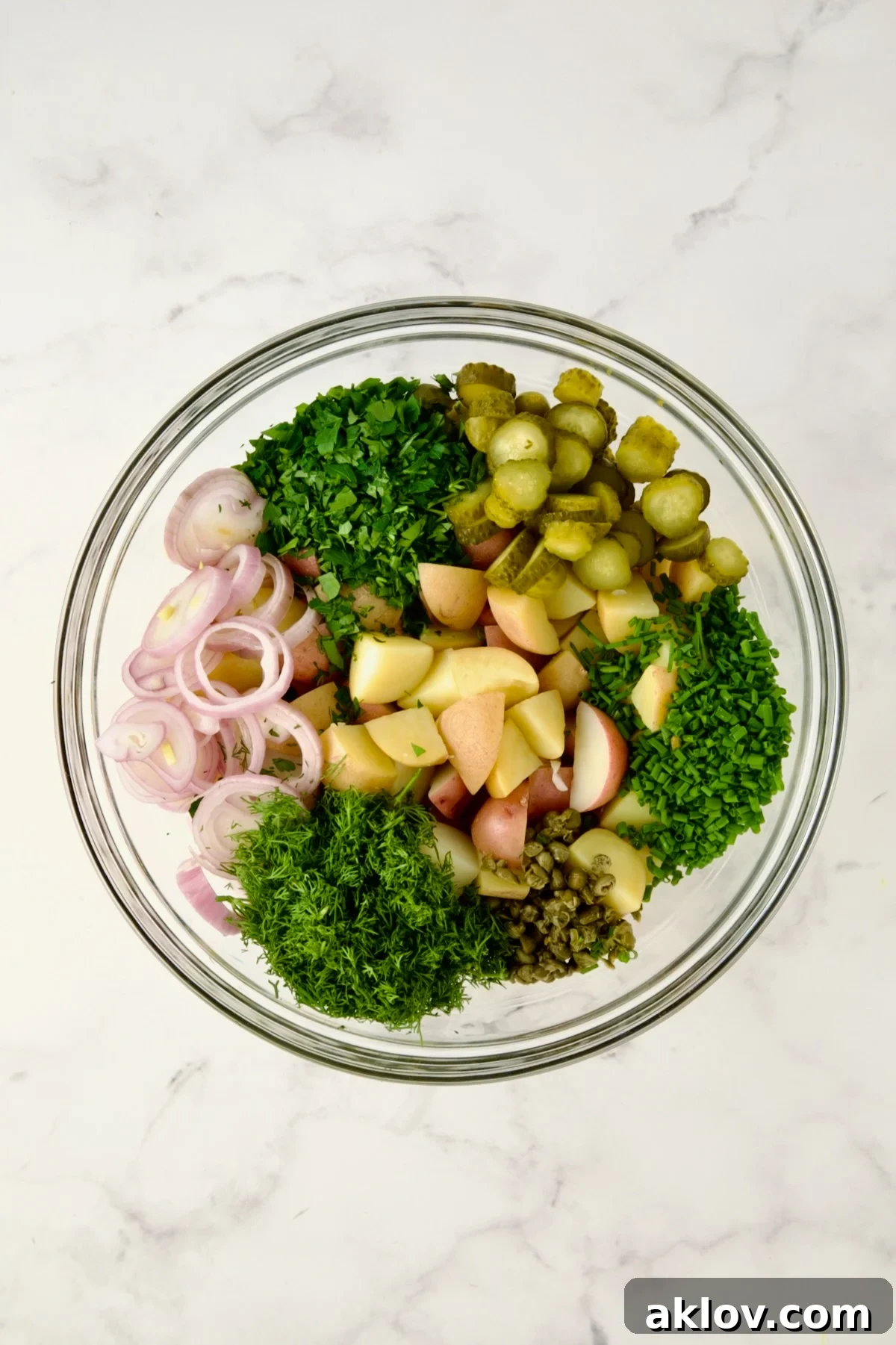 Ingredients for Herb and Vinegar Potato Salad in glass bowl before being mixed together.