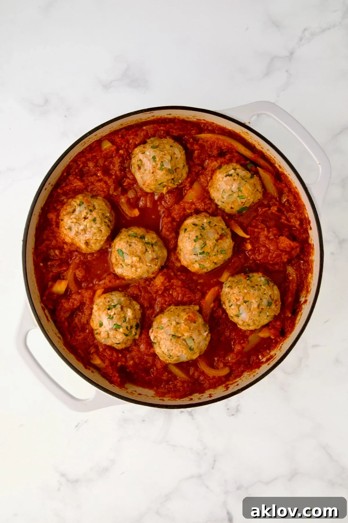 Placing the raw, jumbo-sized chicken meatballs into the simmering tomato sauce.