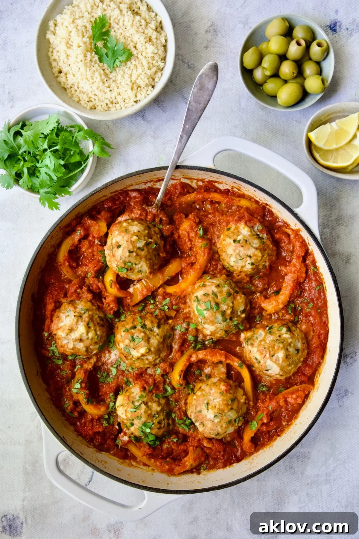 A serving spoon lifting one Harissa Chicken Meatball from the skillet.