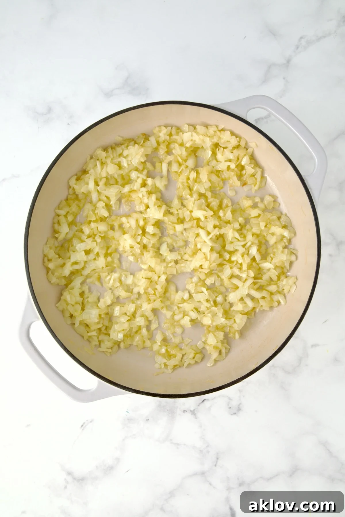 Sautéing chopped onions in a white enameled cast iron skillet.