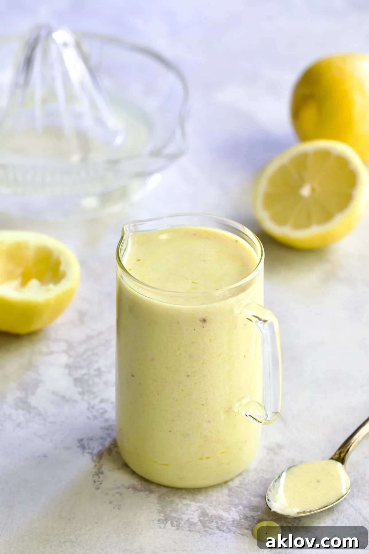 Creamy Lemon Dressing in glass pitcher surrounded by lemon halves with some on a spoon.