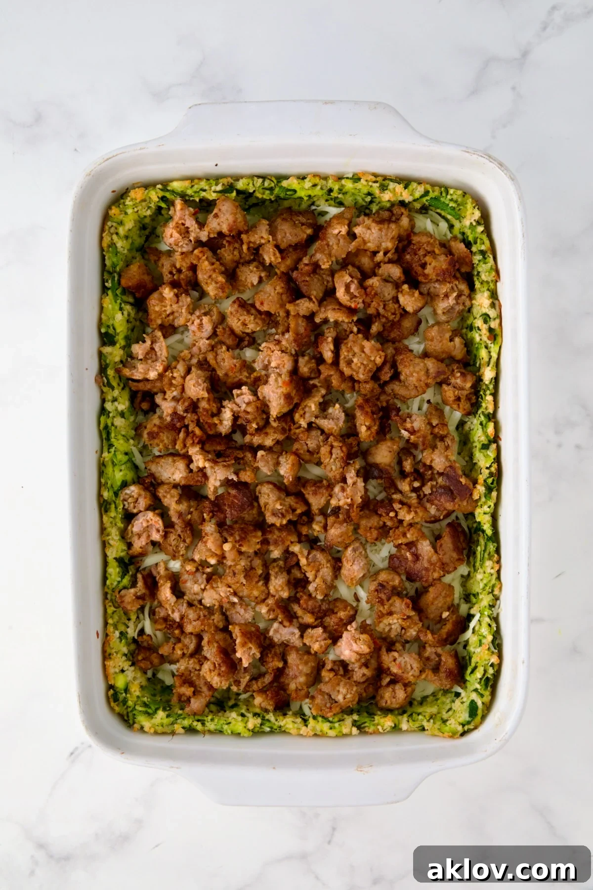 Italian sausage placed over cheese layer in white rectangular baking dish.