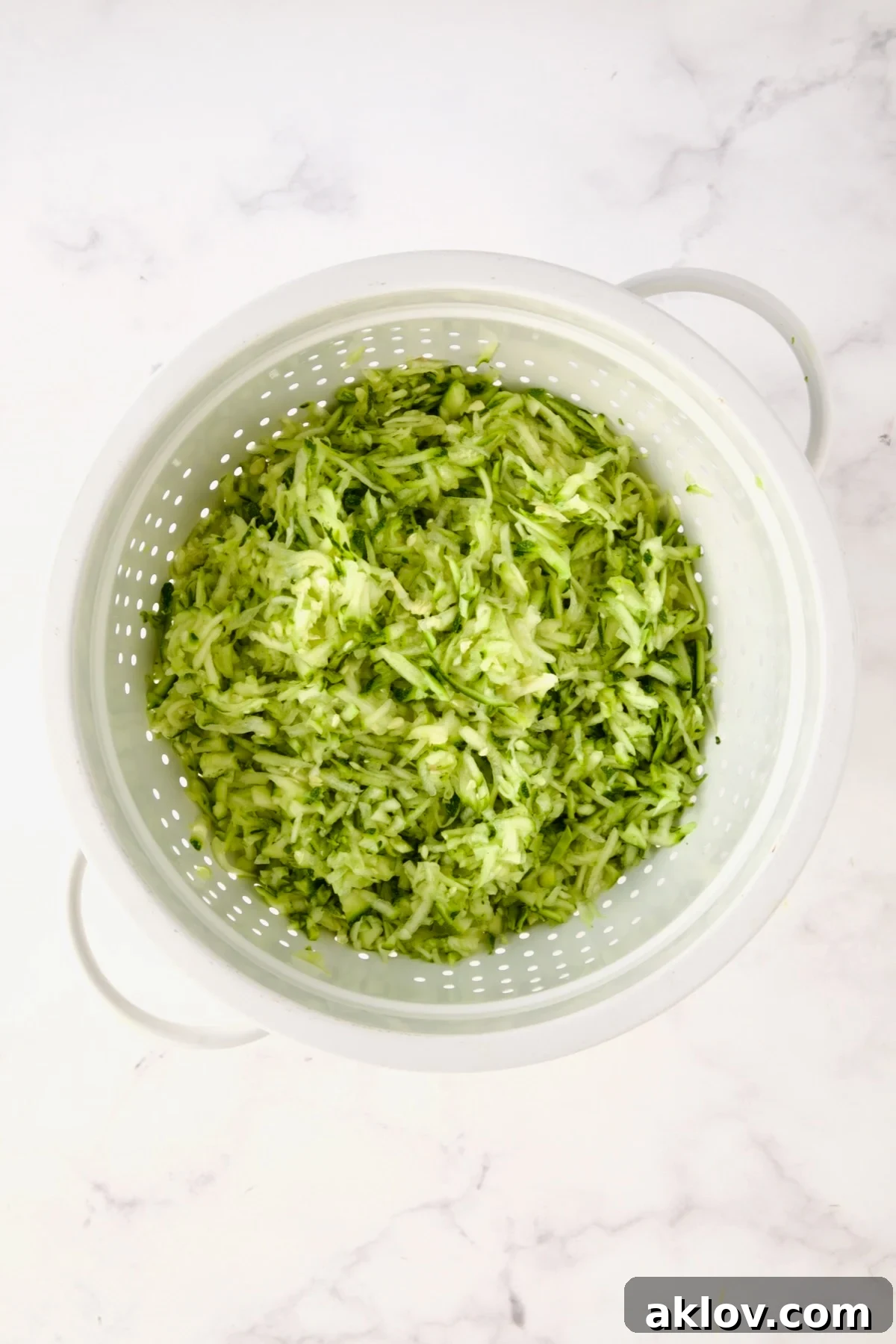 Shredded zucchini in white colander.