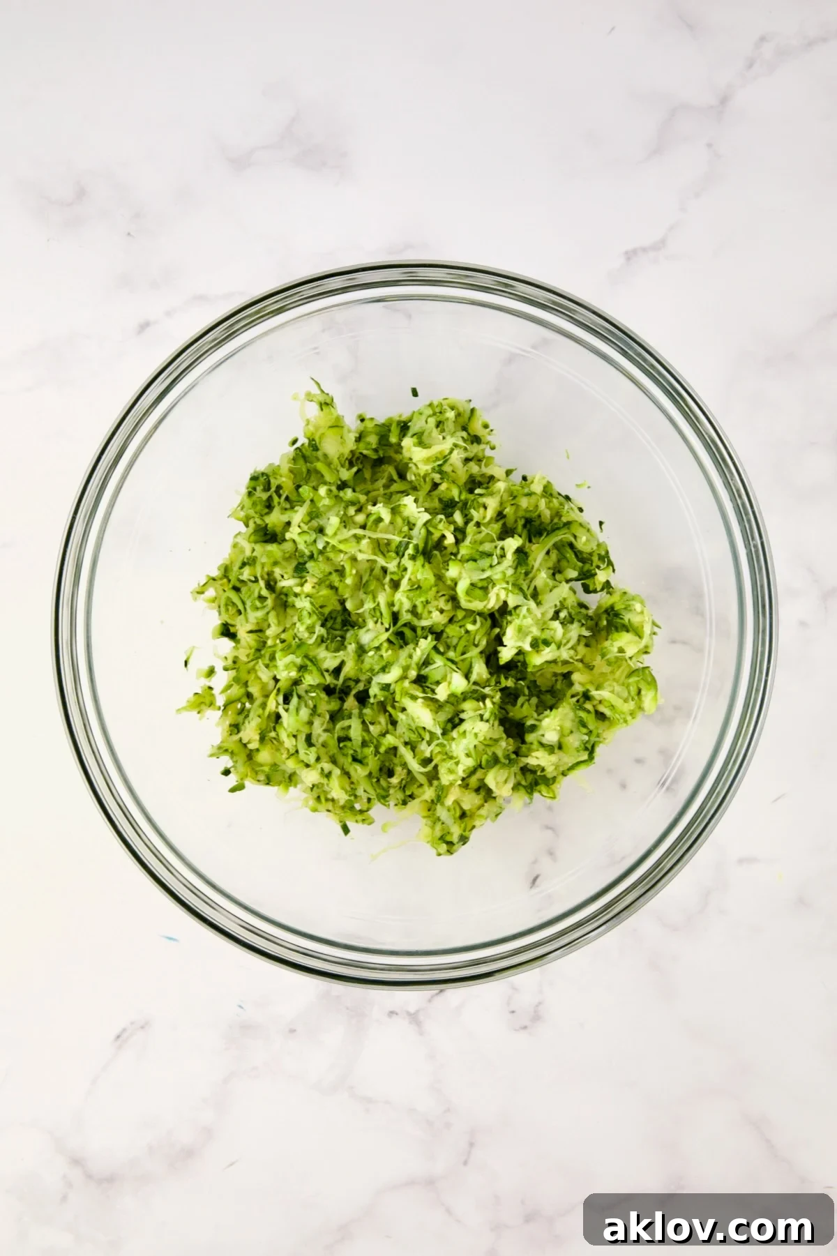 Squeezed shredded zucchini in glass bowl.