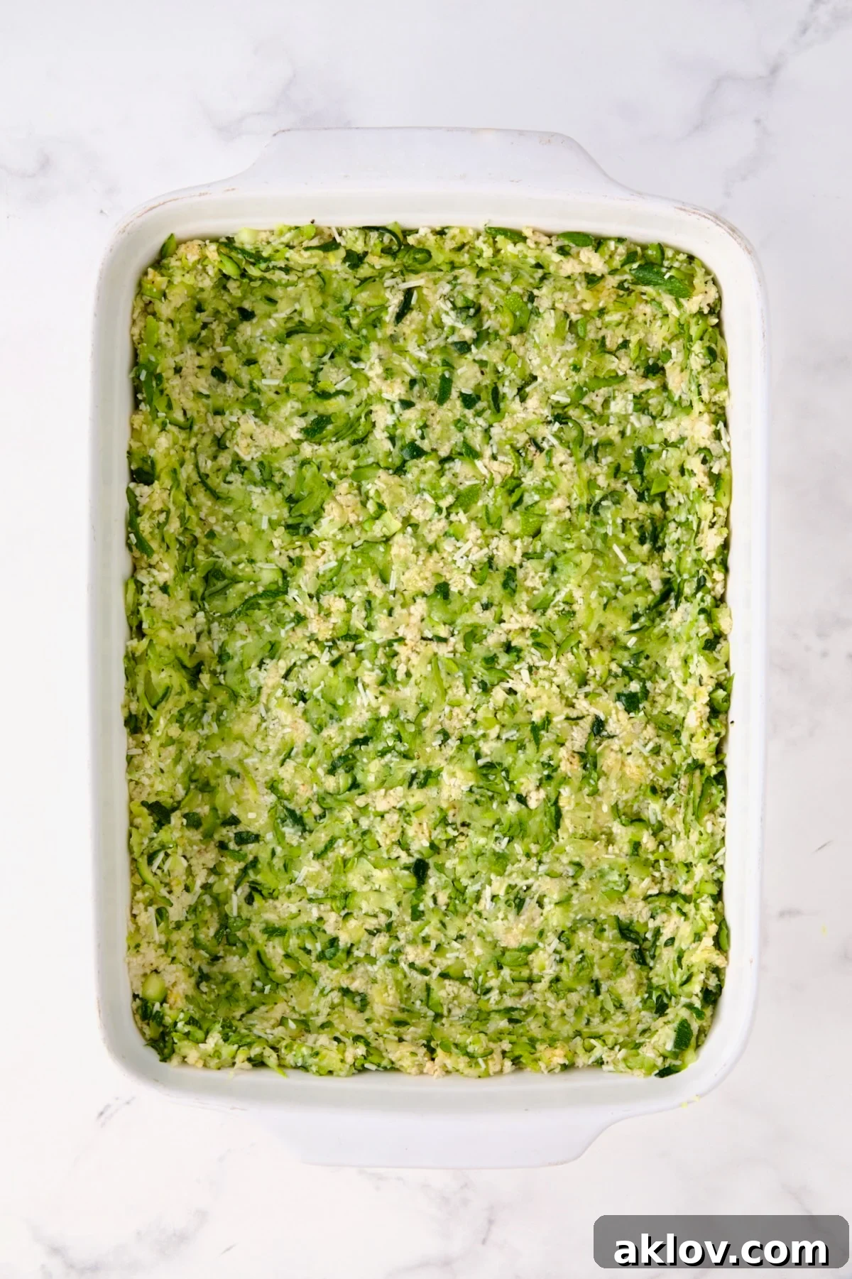 Zucchini crust in white rectangular baking dish before being baked.