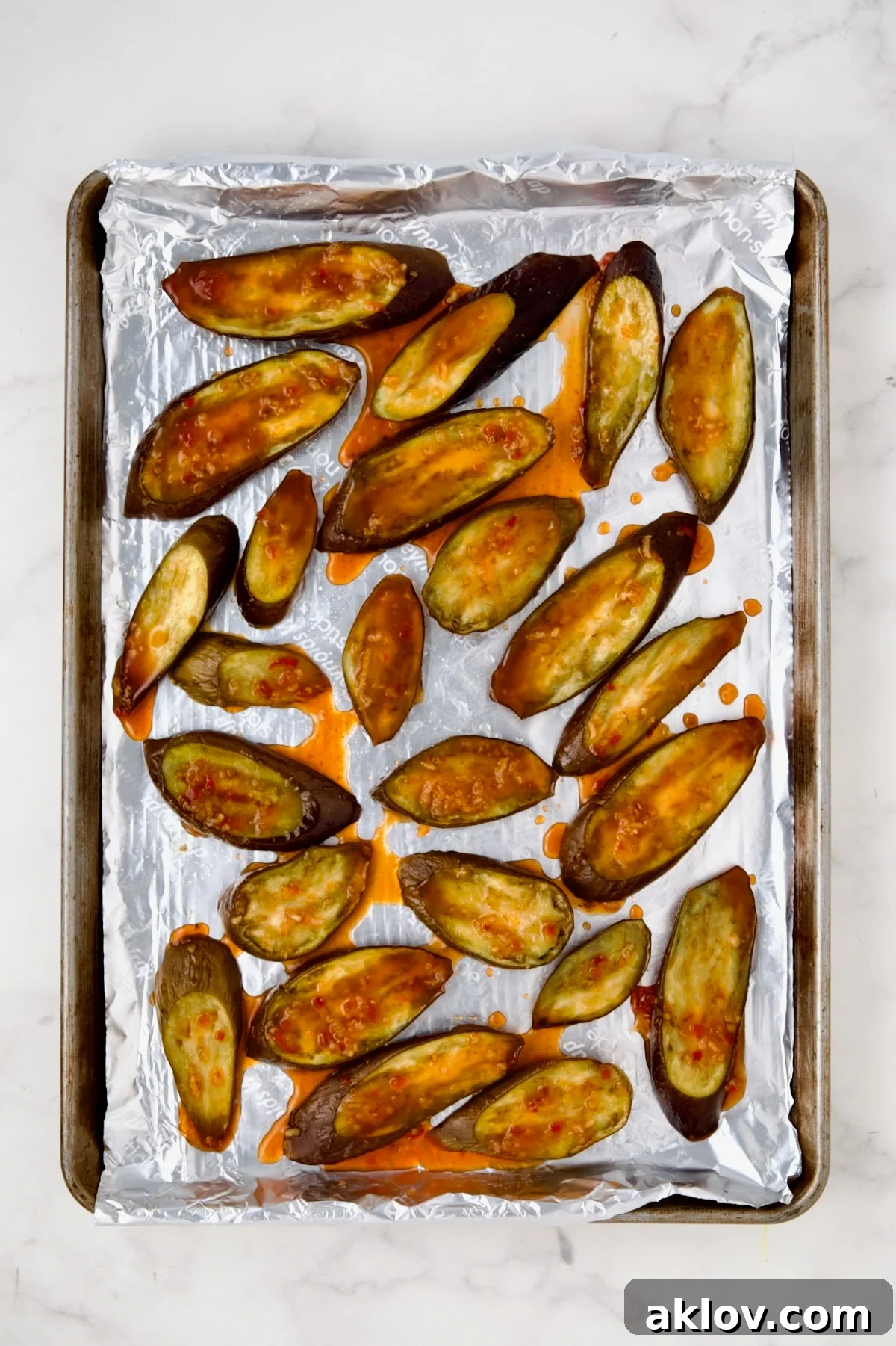 Thai Sweet Chili Glazed Eggplant Recipe 6 Sliced eggplant on aluminum-foil lined rimmed sheet pan after being baked with sauce drizzled over.